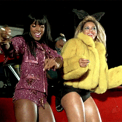🎉 We Like to Party—Bomb Ass Prompt Service Style! 🎉 A high-energy GIF of Beyoncé and Kelly Rowland dancing in the "Party" music video. Beyoncé rocks yellow fur coat & bunny ears, Kelly stuns in sparkly pink outfit. This GIF closes out the Bomb Ass Prompt Service™ page—because AI that slaps deserves a party!
